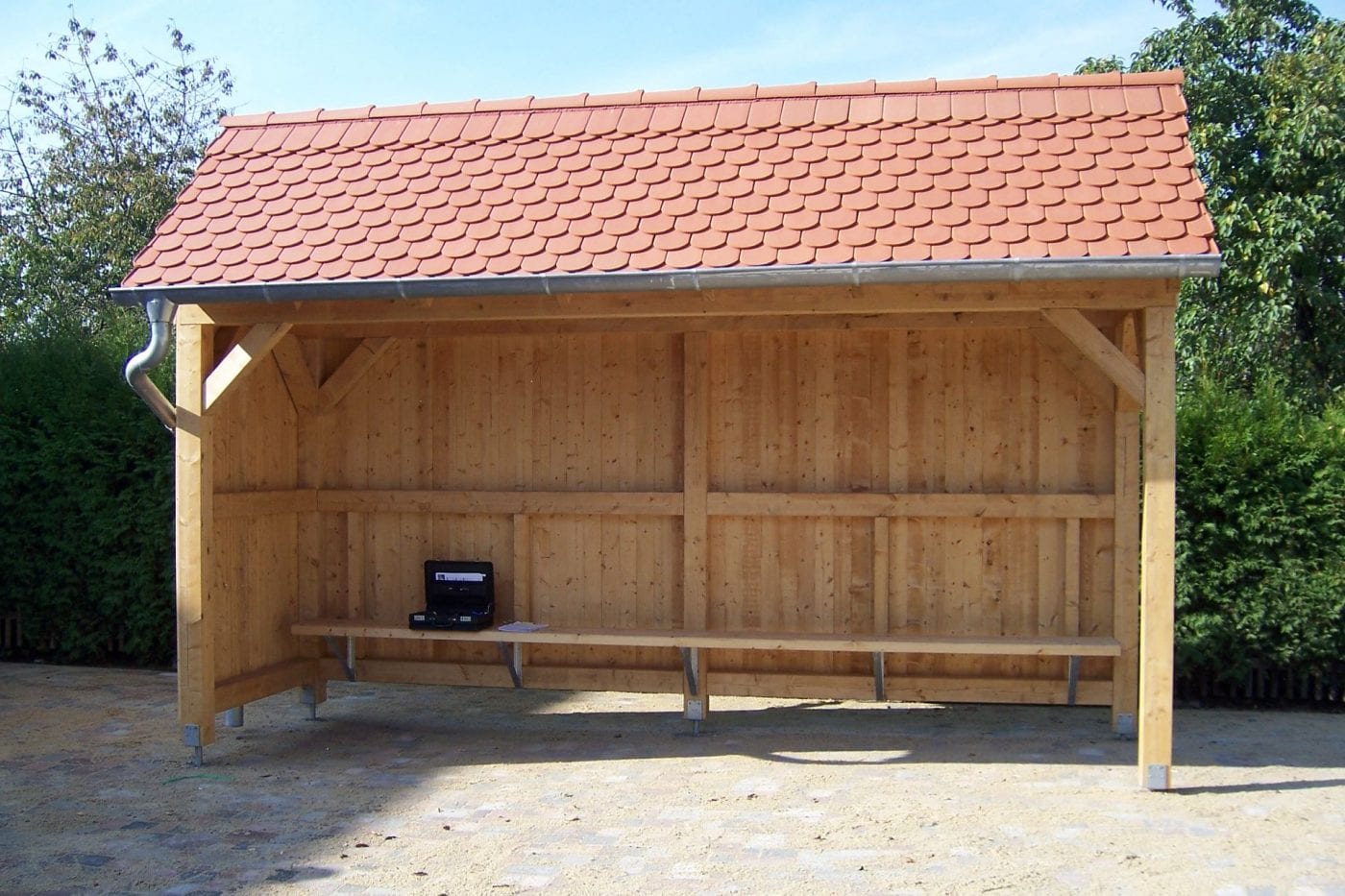 Ein Wartehäuschen aus Holz mit einem roten Dach für eine Bushaltestelle